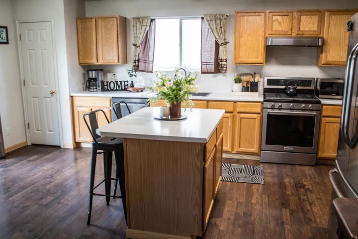 Kitchen featuring wood-finish flooring, light wood cabinetry, white countertops, a central island, and stainless steel appliances