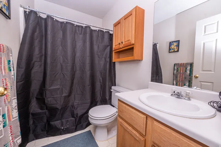 Bathroom featuring a single vanity with a white countertop, wood-finish cabinetry, a large mirror, a toilet, and a shower/tub combination