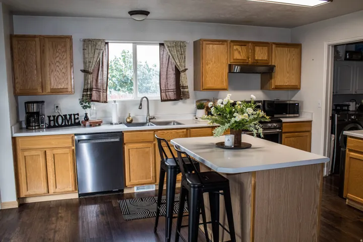 Kitchen featuring wood-finish cabinetry, light-toned countertops, stainless steel appliances, a center island, and wood-finish flooring