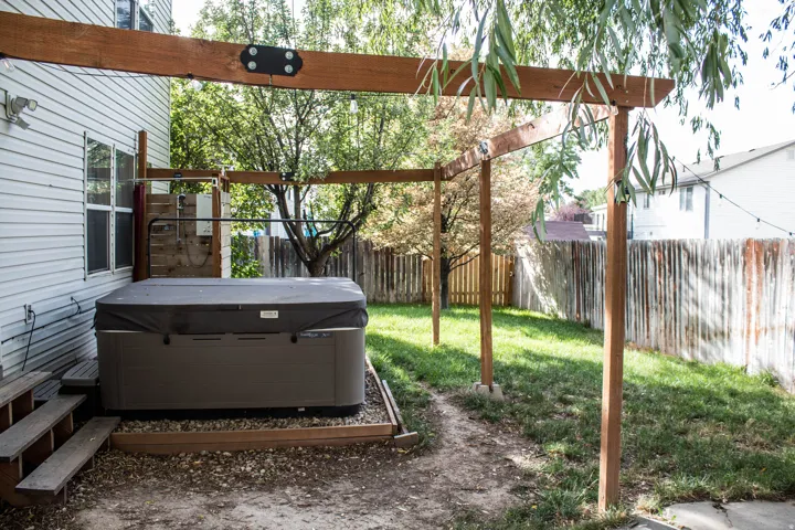 Outdoor spa area with a wood pergola structure, slatted wood privacy wall, and a multi-level wood deck