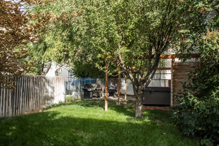 Manicured lawn with mature trees, corrugated metal fencing, and built-in hot tub
