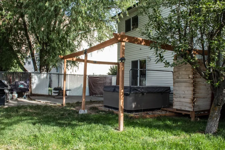 Pergola structure over a hot tub, concrete patio, and mature trees in a fenced yard