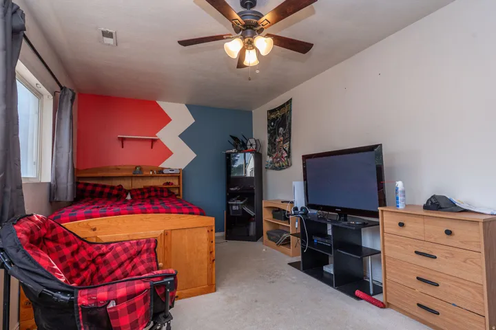 Carpeted bedroom featuring a ceiling fan with integrated lighting, a window, and painted walls