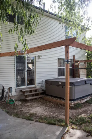 Vinyl siding exterior with a ground-level patio featuring a hot tub, a wooden pergola, and sliding glass door access