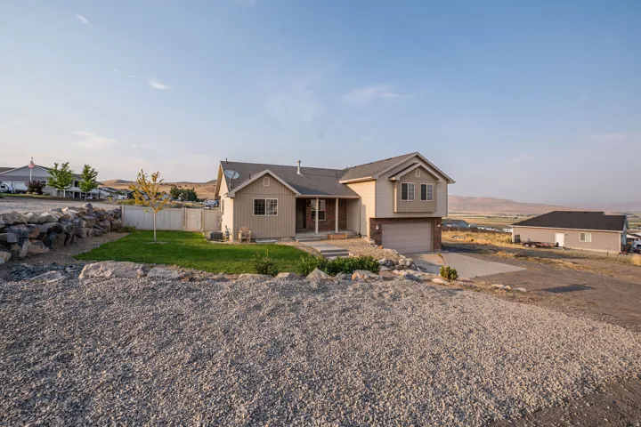 Exterior featuring a two-story design, an attached garage, a gravel driveway, a partial lawn, and a retaining wall
