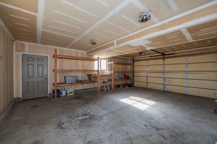 Attached garage with concrete flooring, overhead lighting, and built-in wood shelving