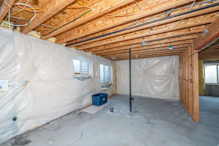 Unfinished basement with exposed wood framing, concrete flooring, and multiple windows