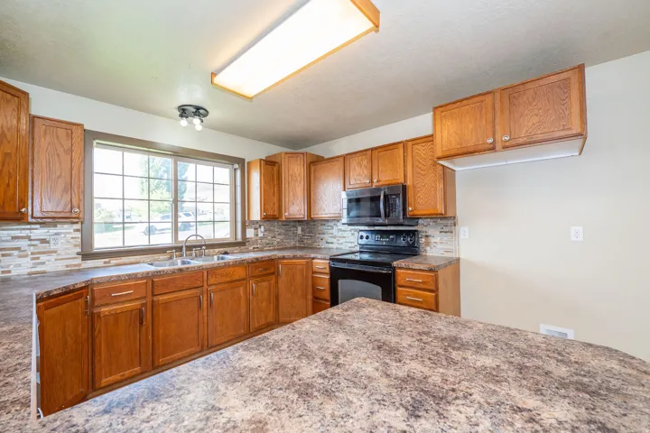 Kitchen with wood-finish cabinetry, patterned countertops, and a mosaic tile backsplash