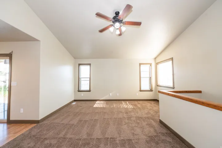 Vaulted ceiling with a ceiling fan, carpeted flooring, multiple windows with blinds, wood-finish flooring, and a wood-finish handrail