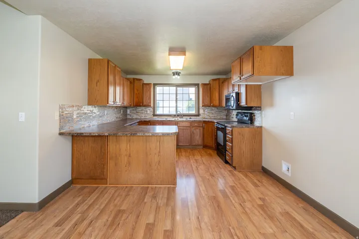 Kitchen featuring wood-finish flooring, wood cabinetry, stone-look countertops, and a tile backsplash