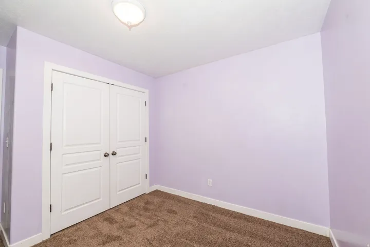 Recessed bi-fold closet doors with panel detailing, flush mount ceiling light fixture, and brown carpet flooring