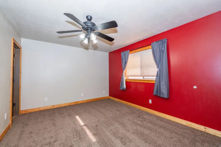 Ceiling fan with integrated lighting, window with blinds and drapes, wood-finish trim, carpeted flooring, and a solid door