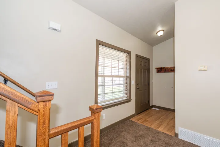 Entryway featuring a wood-finish door, a window with blinds, a wood-finish coat rack, and carpeted flooring with a wood-finish inlay