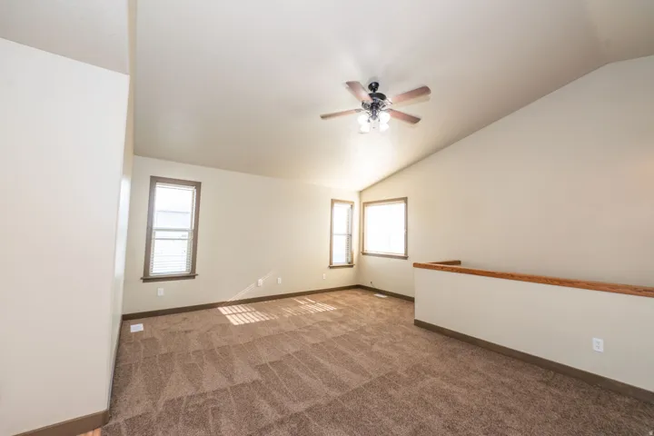 Vaulted ceilings, contemporary ceiling fan, multiple windows, and carpeted flooring