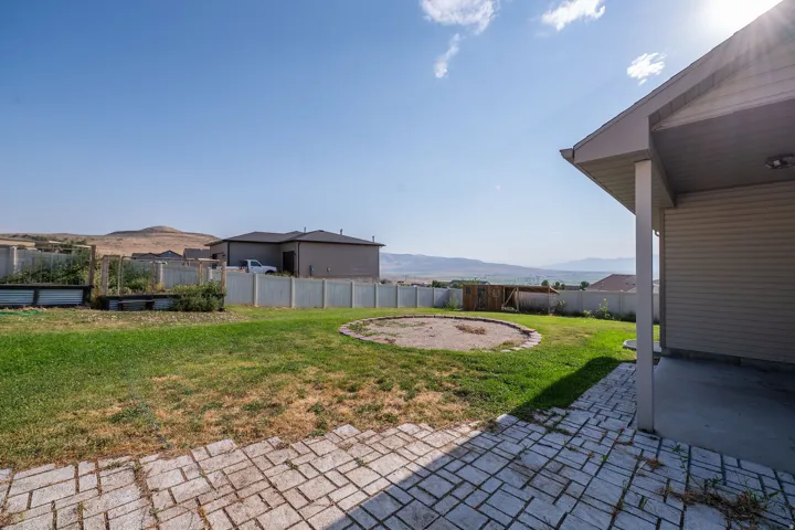 Expansive backyard featuring a stone paver patio, a covered concrete patio, a manicured lawn, and raised garden beds