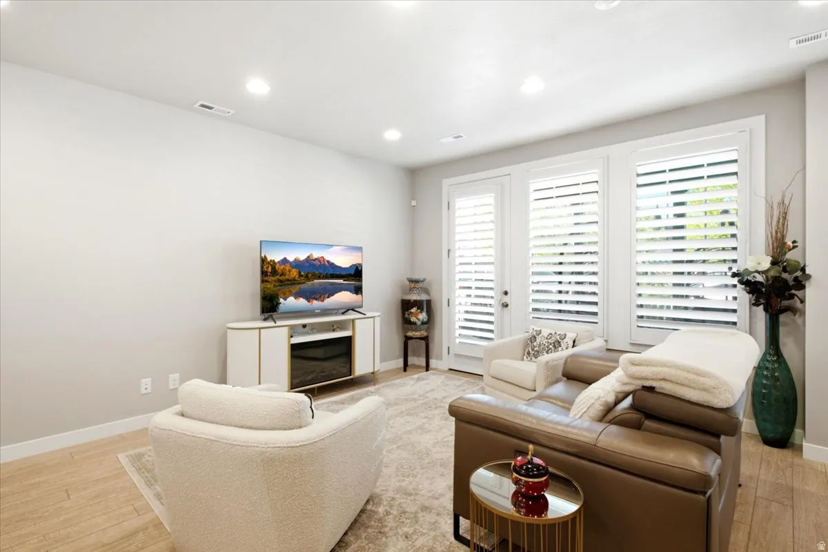 Recessed lighting, wood-finish flooring, white walls, and a glass-paneled door with plantation shutters
