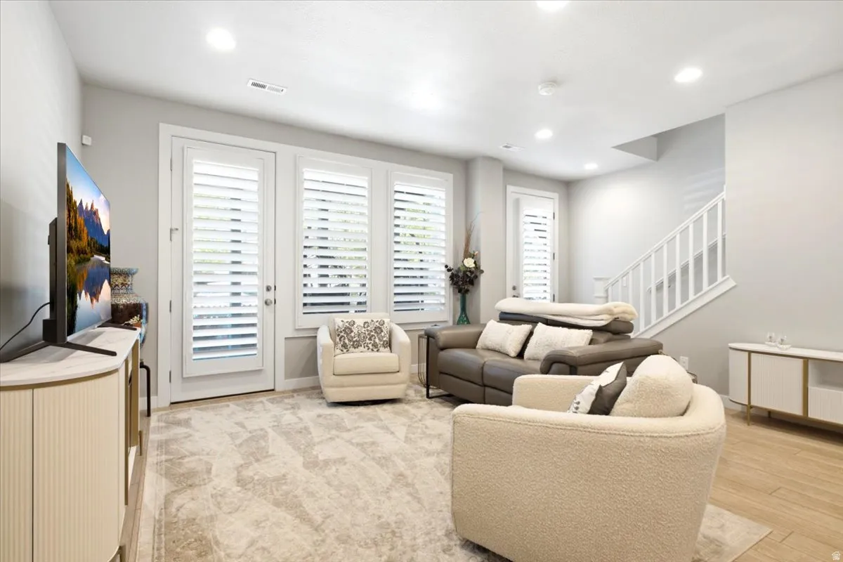 Recessed lighting, white plantation shutters, white painted staircase with railing, wood-finish flooring, and light-toned carpeting