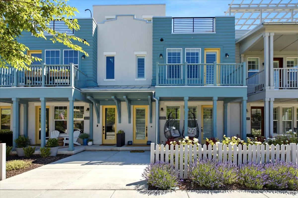 Multi-level townhome featuring a white picket fence, a lower-level patio, an upper-level balcony, a rooftop deck, and vibrant yellow doors
