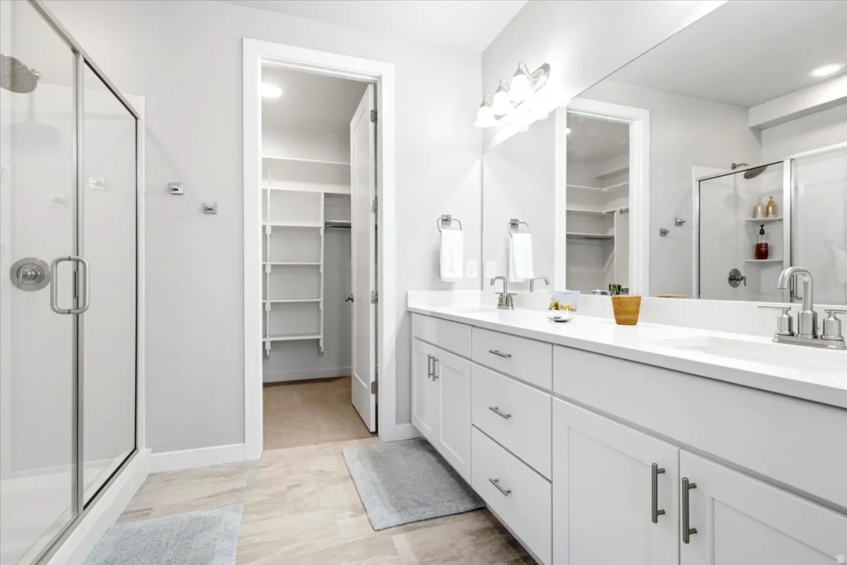 Spacious bathroom featuring a glass-enclosed shower, dual vanities with white countertops, expansive mirrors, and a walk-in closet with built-in shelving