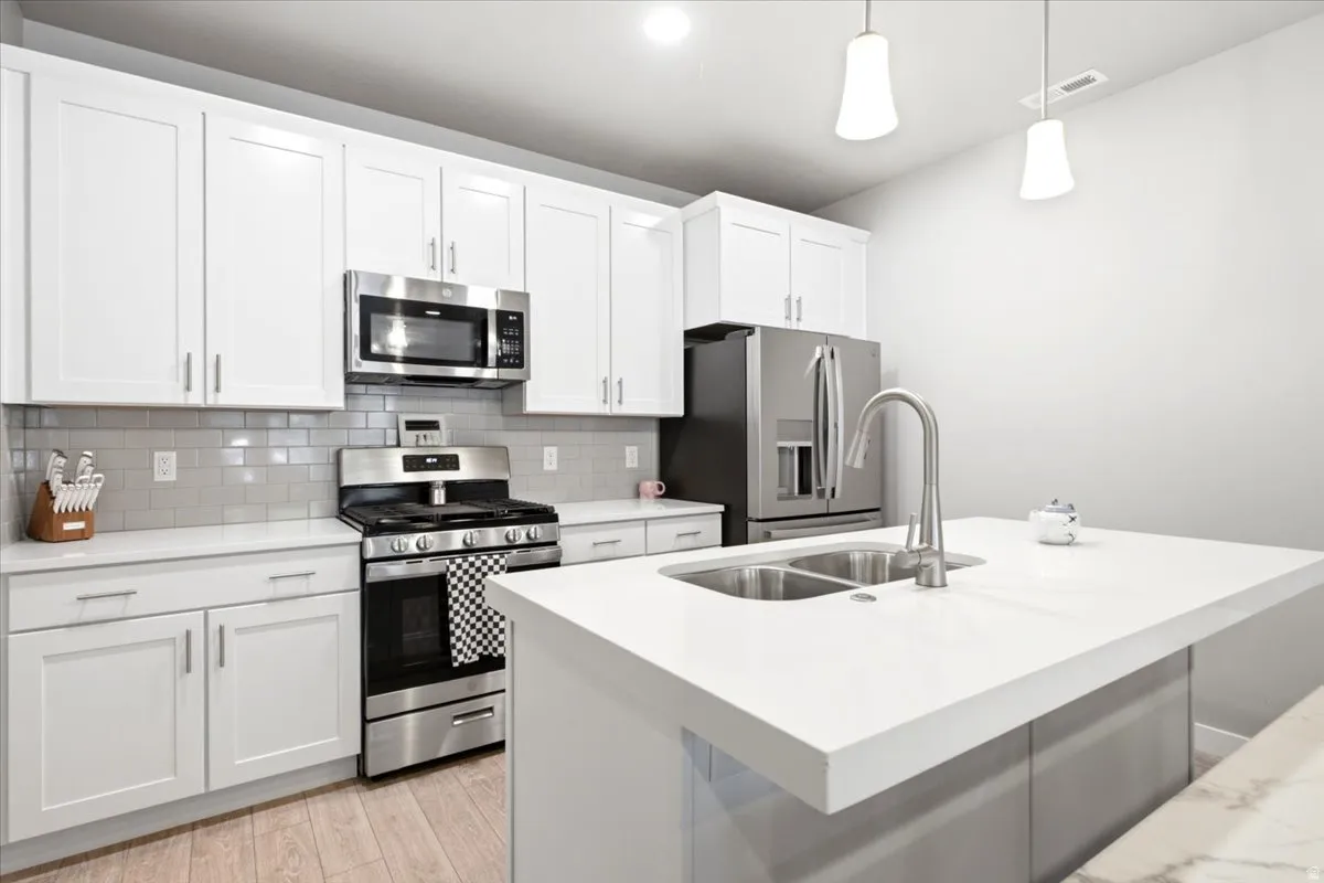 White shaker cabinetry, stainless steel appliances, light wood-finish flooring, white countertops, and a dual basin undermount sink with a gooseneck faucet