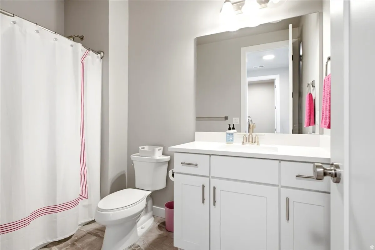 White vanity with brushed nickel hardware, solid surface countertop, integral sink, wall-mounted mirror, and overhead lighting
