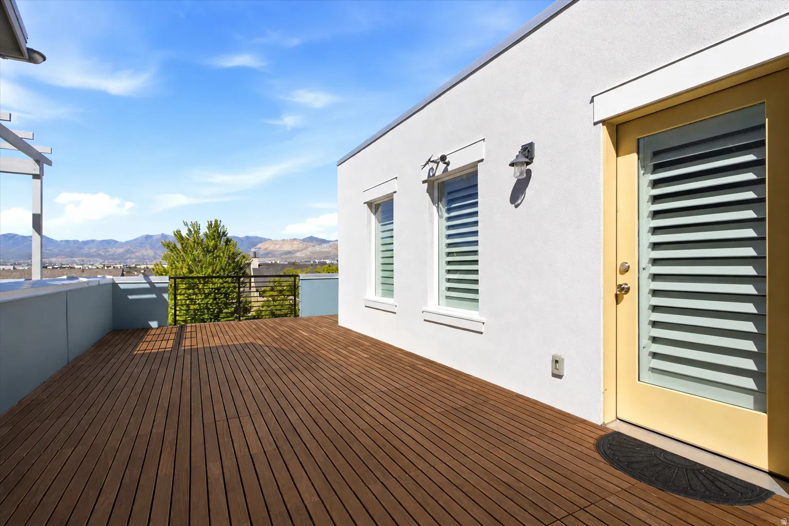 Expansive rooftop deck featuring wood-finish decking, stucco exterior, mounted sconces, and louvered window treatments. (Wood stain has been enhanced)