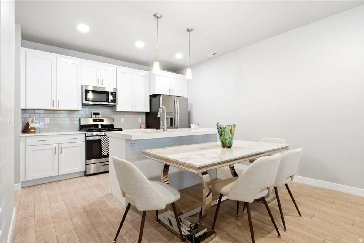 Modern kitchen featuring white cabinetry, stainless steel appliances, light wood-finish flooring, recessed lighting, and a kitchen island with pendant lighting