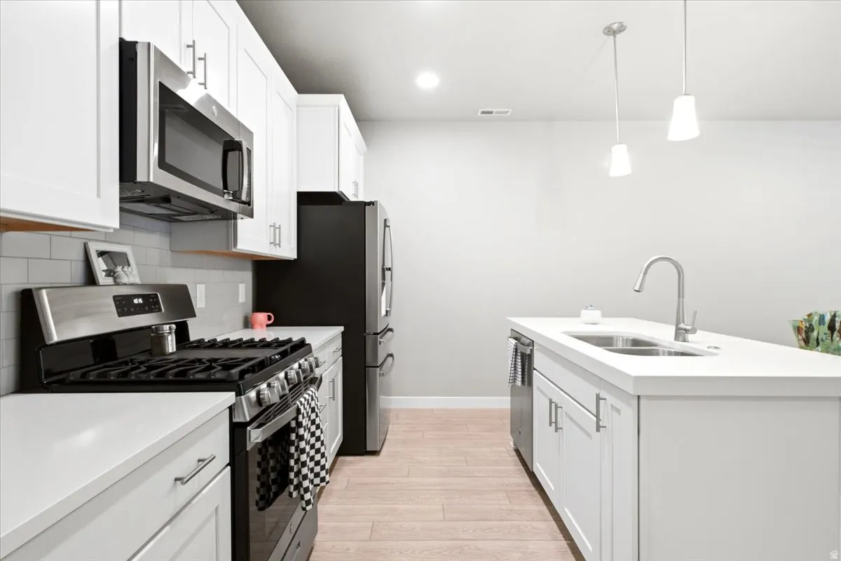 Modern kitchen featuring white cabinetry, light-toned countertops, stainless steel appliances, and a subway tile backsplash