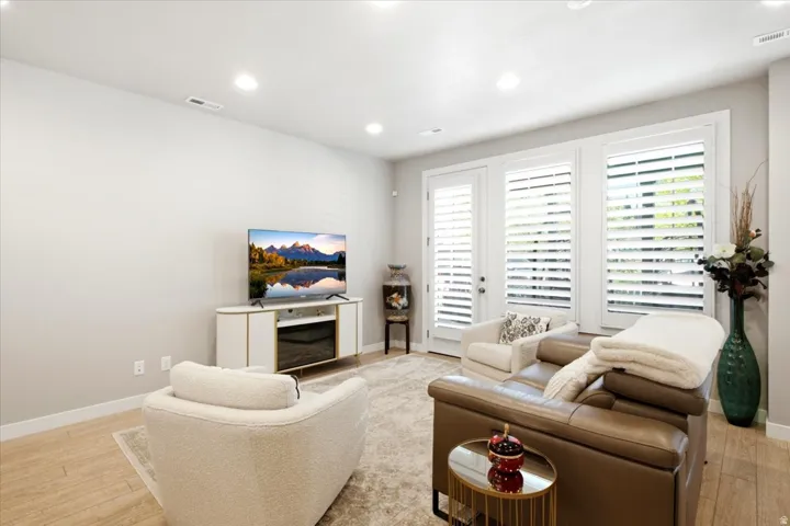 Recessed lighting, wood-finish flooring, white walls, and a glass-paneled door with plantation shutters