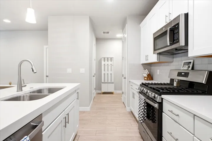 Kitchen featuring white cabinetry, stainless steel appliances, a double basin sink, and wood-finish flooring