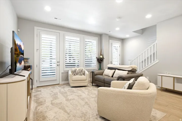Recessed lighting, white plantation shutters, white painted staircase with railing, wood-finish flooring, and light-toned carpeting