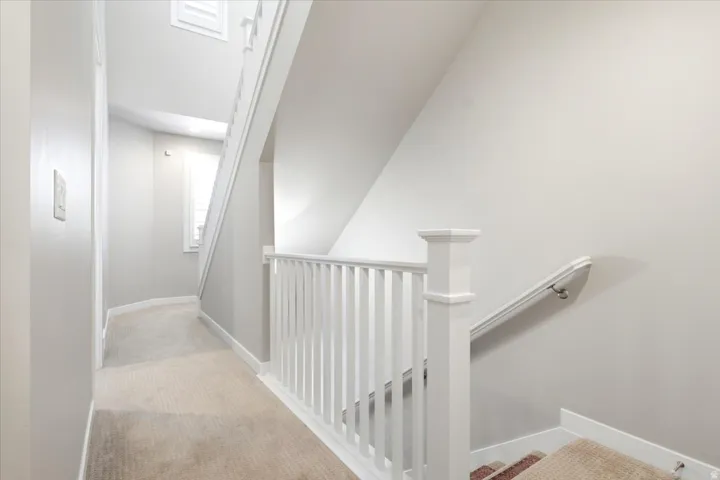 Carpeted hallway with white trim, white spindle railing, and a window with white louvered shutters