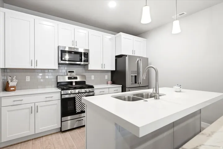 White shaker cabinetry, stainless steel appliances, light wood-finish flooring, white countertops, and a dual basin undermount sink with a gooseneck faucet