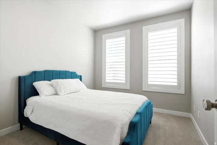 Dual windows with white plantation shutters, neutral wall color, and carpeted flooring