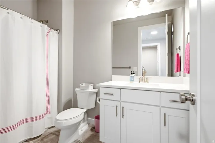 White vanity with brushed nickel hardware, solid surface countertop, integral sink, wall-mounted mirror, and overhead lighting
