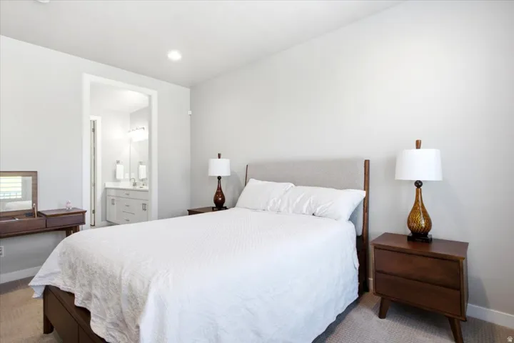Recessed ceiling lighting, light neutral wall color, carpet flooring, bathroom vanity with dual sinks, and wall-mounted light fixtures