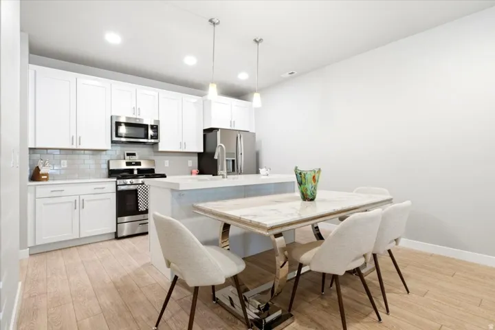 Modern kitchen featuring white cabinetry, stainless steel appliances, light wood-finish flooring, recessed lighting, and a kitchen island with pendant lighting