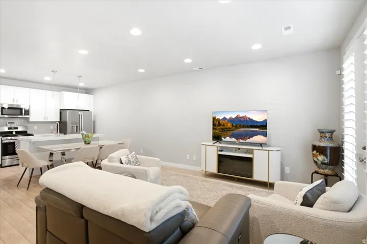 Open-concept living space featuring wood-finish flooring, recessed lighting, white cabinetry, stainless steel appliances, and plantation shutters