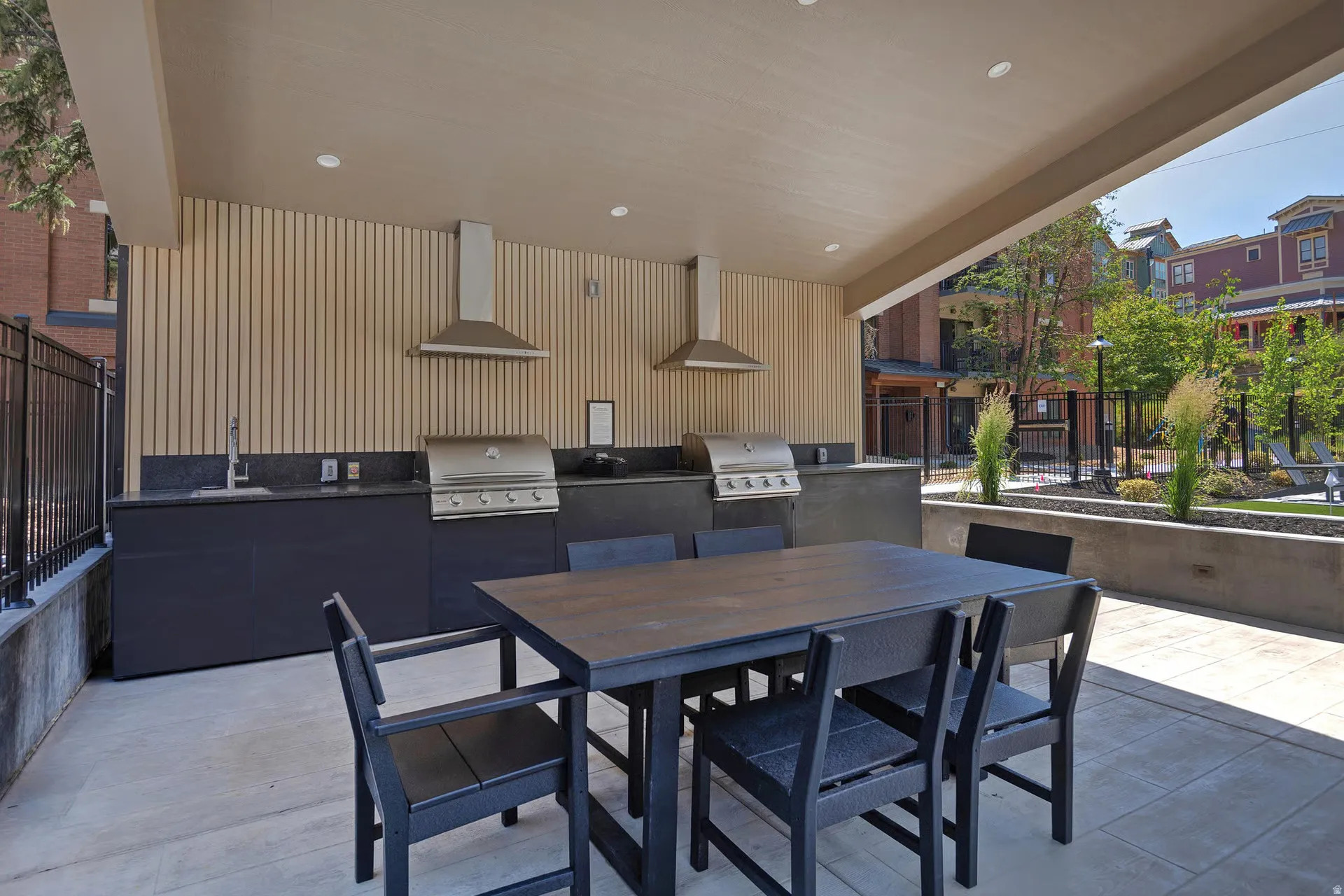 Covered outdoor kitchen featuring two built-in grills, stainless steel range hoods, and a stainless steel sink