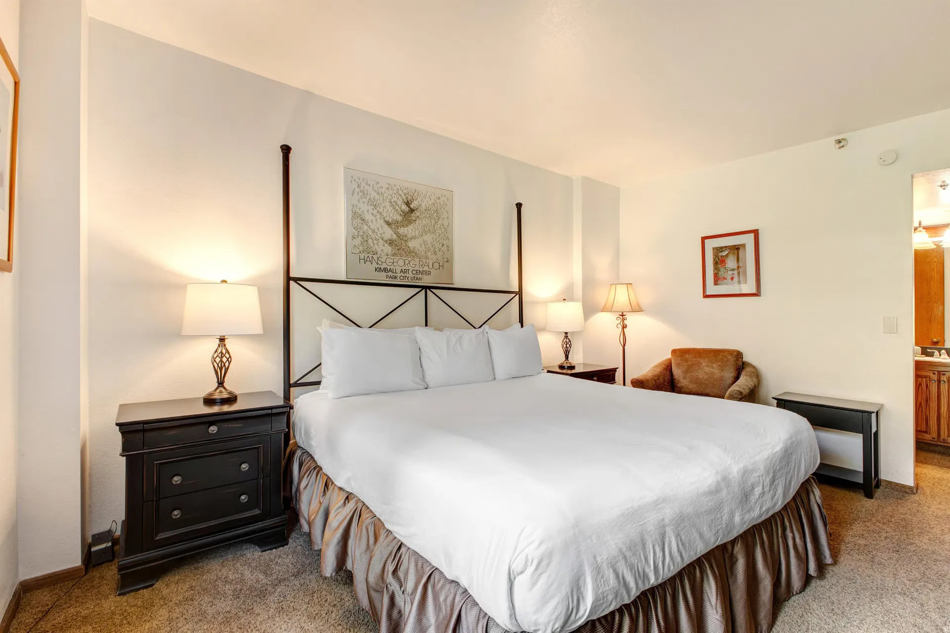 Spacious room featuring a four-poster bed frame, neutral-toned carpeting, and white wall finishes