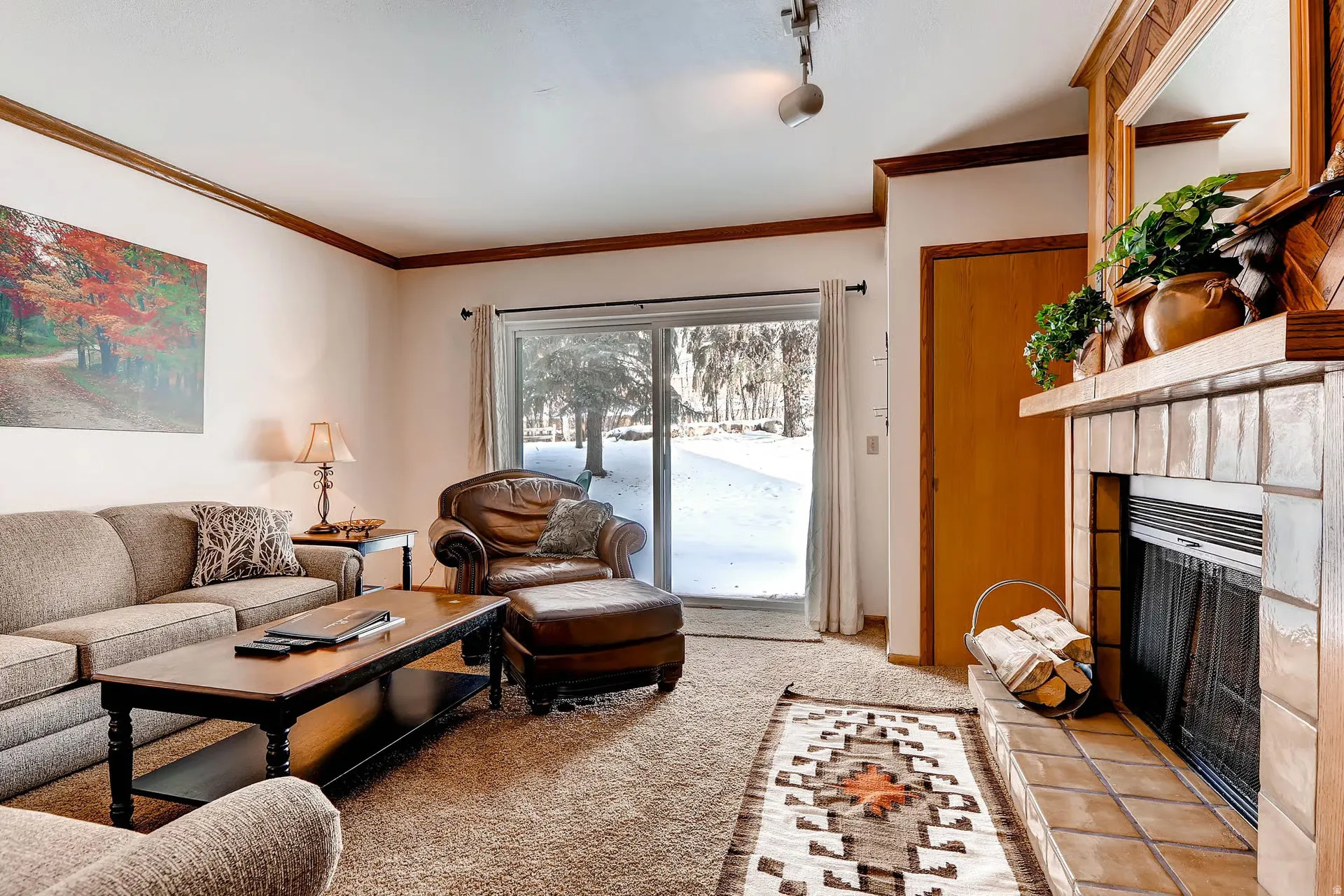 Living area featuring a tiled fireplace with wood mantel, sliding glass door, and crown molding
