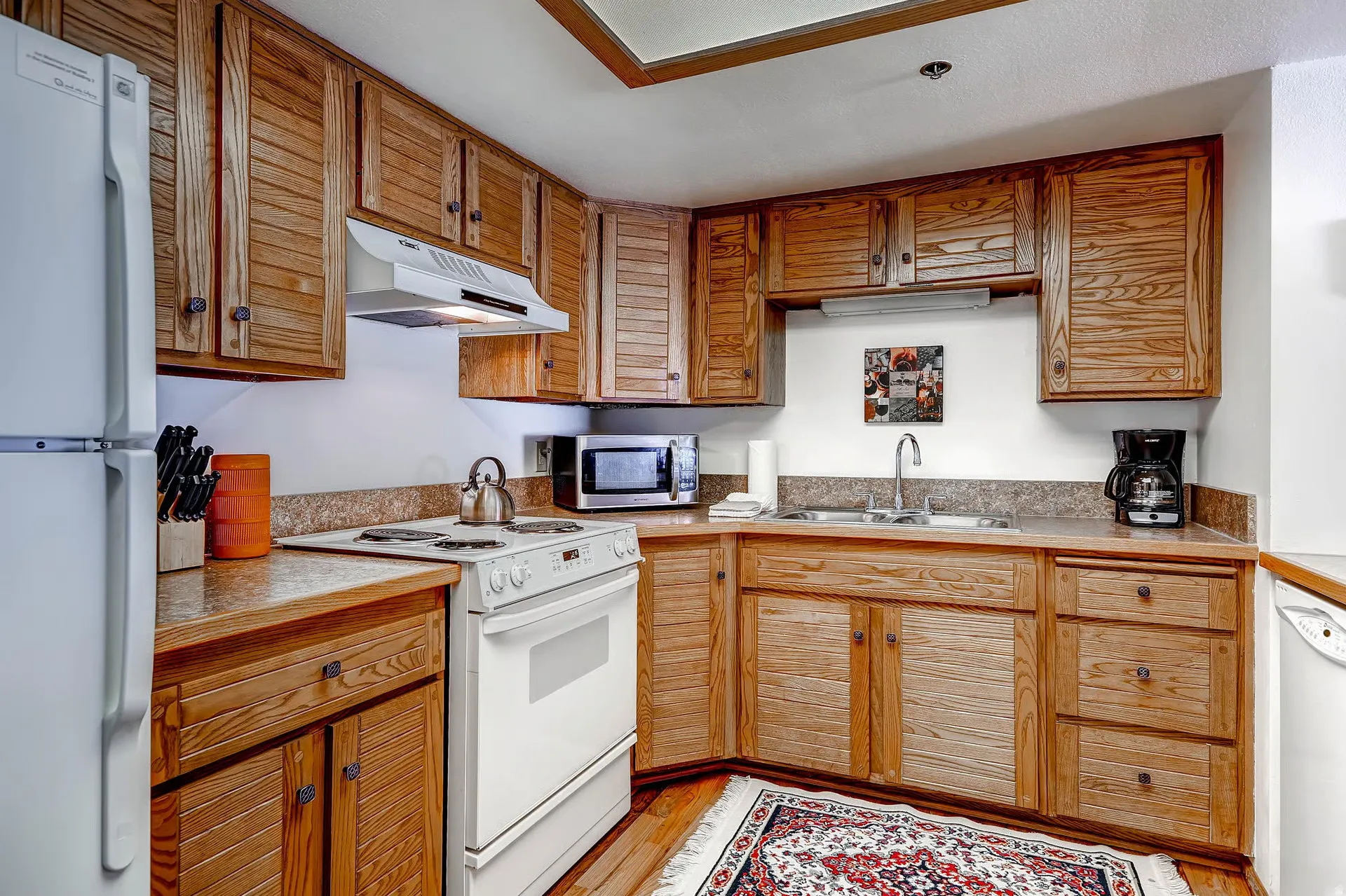 Efficient kitchen featuring wood cabinetry, white appliances, durable countertops, and wood-finish flooring