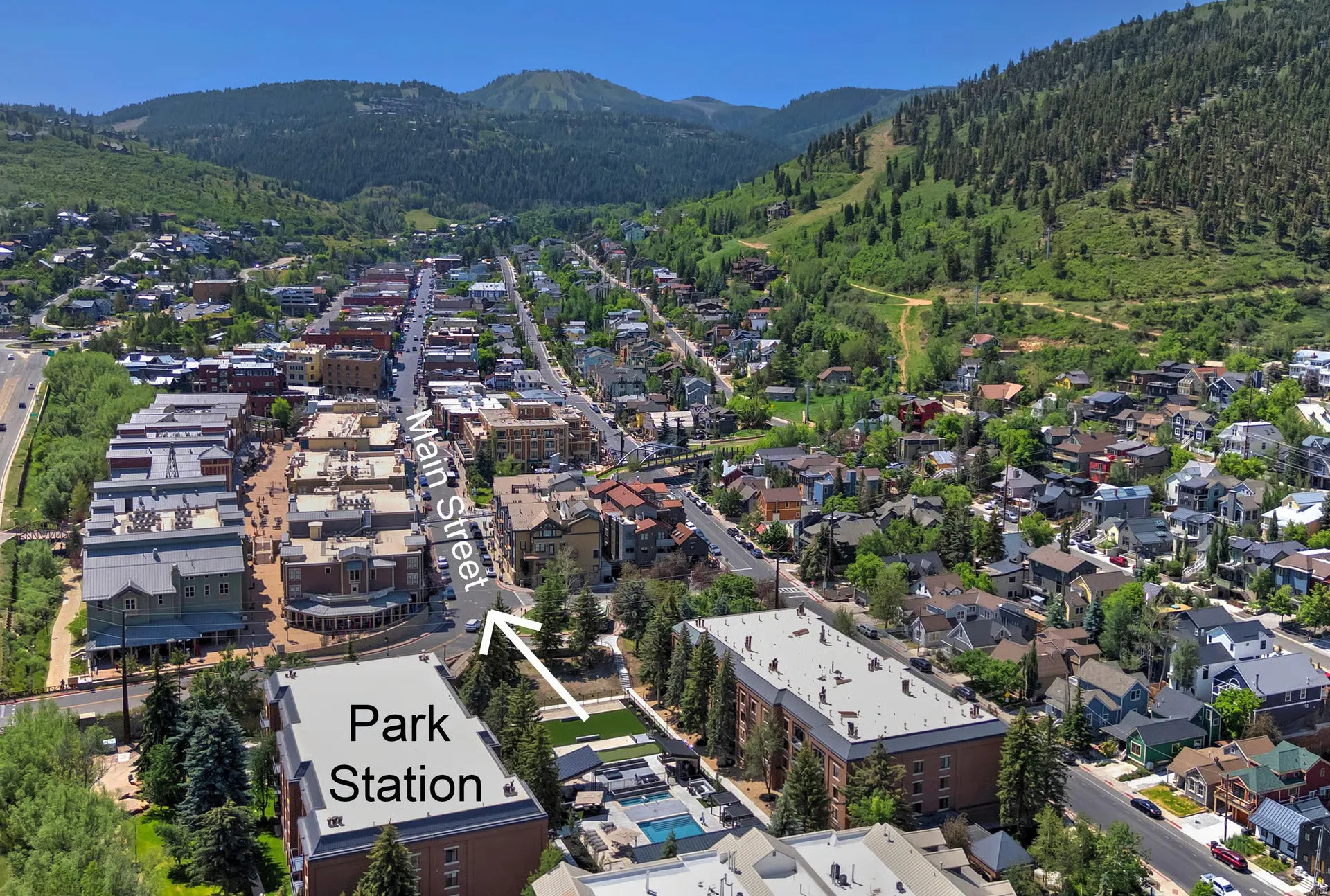 Aerial perspective showcasing a vibrant town with a central Main Street, residential areas, and surrounding green mountains