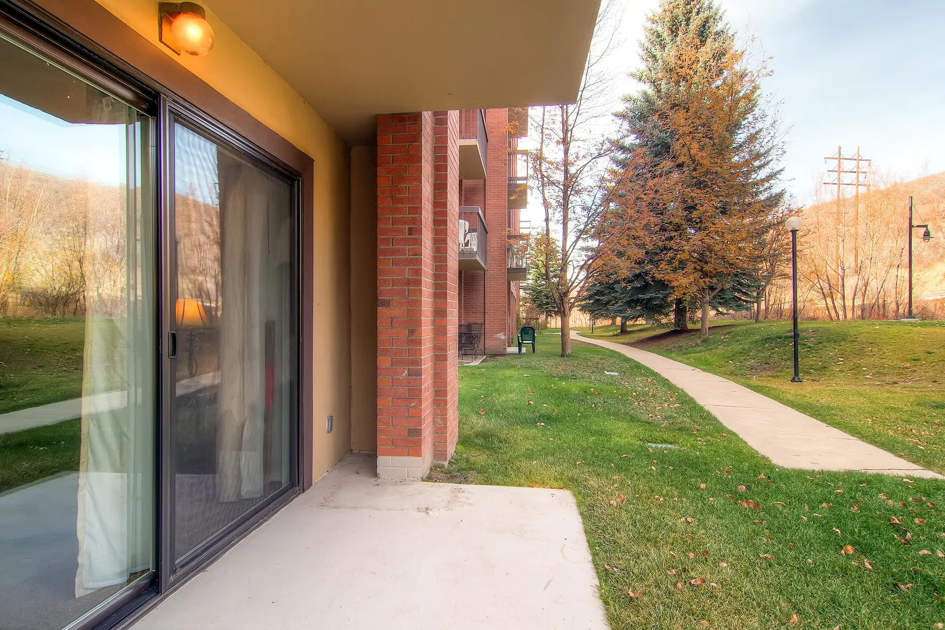 Ground-level patio featuring a sliding glass door with screen, exterior wall light, and brick column accents