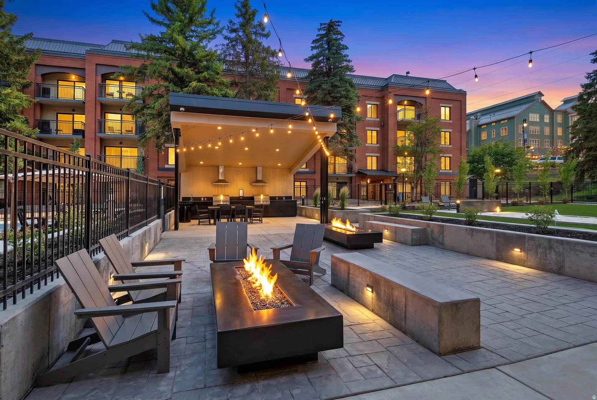 Outdoor patio featuring a modern fire pit, an adjacent covered outdoor kitchen with built-in grills, and string lighting