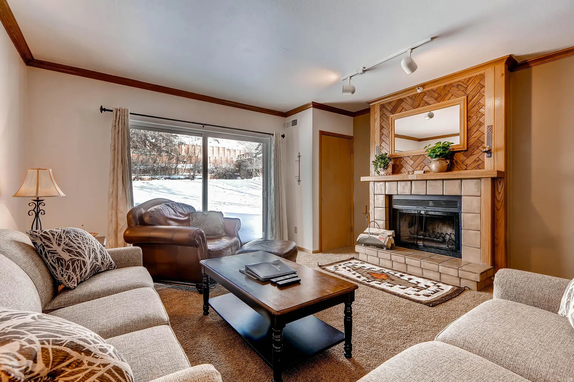 Living area featuring a stone-clad fireplace with wood surround, track lighting, and a large sliding glass door