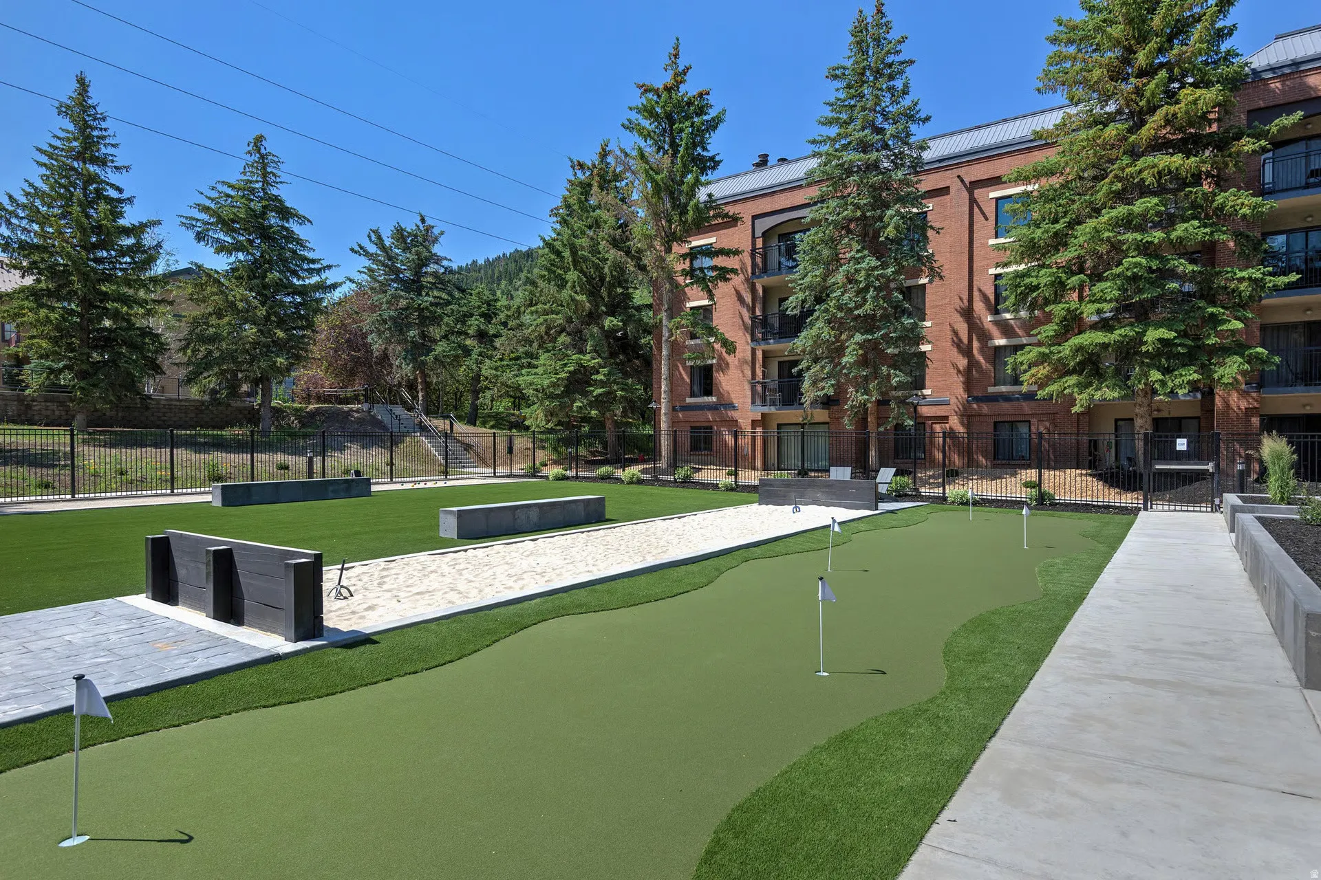 Putting green with multiple holes, artificial turf, and adjacent sand court