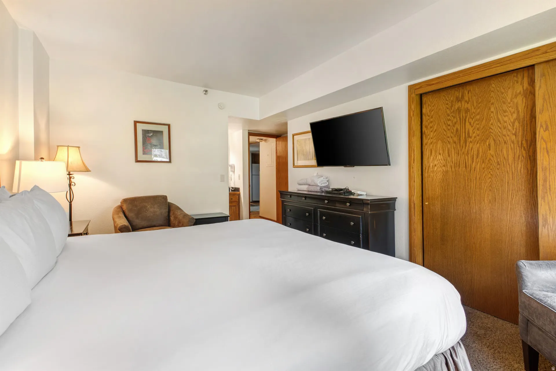 Carpeted interior space featuring a built-in wood-finish closet with sliding doors, a wall-mounted flat-screen television, a dark wood-finish dresser with multiple drawers, and a ceiling-mounted light fixture