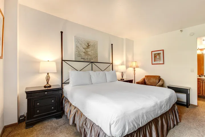 Spacious room featuring a four-poster bed frame, neutral-toned carpeting, and white wall finishes