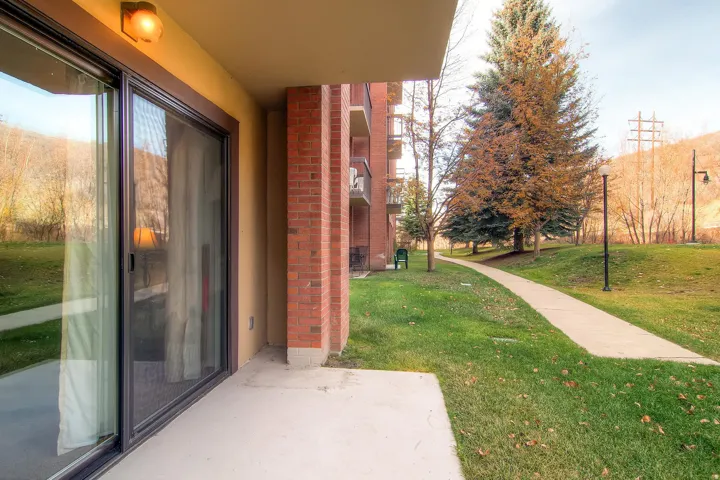 Ground-level patio featuring a sliding glass door with screen, exterior wall light, and brick column accents